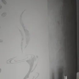 Ściana z dekoracyjnym malowaniem szablonowym przedstawiającym filiżankę kawy i ziarna, obok ściana wykończona w odcieniach szarości, w tle widoczne świece.