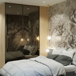 Holistic Studio Julia Ulikowska - Sypialnia w mieszkaniu inwestycyjnym w Krakowie: łóżko z szarą pościelą, szafa z lustrzanymi drzwiami i tapeta z motywem kwiatowym w odcieniach beżu i szarości.