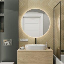 Holistic Studio Julia Ulikowska - Nowoczesna łazienka z okrągłym lustrem podświetlanym LED, drewnianą szafką pod umywalką nablatową i czarną armaturą, widoczna pralka i dekoracyjne płytki na ścianie.