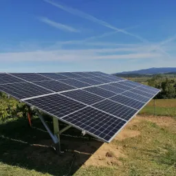 Panel słoneczny zamontowany na łące z widokiem na góry i błękitne niebo z chmurami.