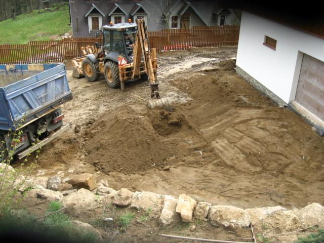 Przygotowanie terenu pod budowę tarasu: koparka i wywrotka na działce, widoczne wyrównywanie ziemi i kamienne obrzeże. Prace ziemne w toku.