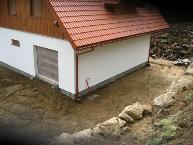 Przygotowanie terenu pod budowę tarasu przy budynku z brązową stolarką okienną i czerwoną dachówką. Widoczne wykopane podłoże i kamienne obrzeże.