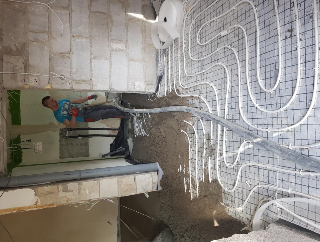 Pracownik rozprowadza wylewkę na ogrzewaniu podłogowym w pomieszczeniu w trakcie prac wykończeniowych.