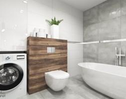Nowoczesna łazienka z białą wolnostojącą wanną, pralką obok zabudowy z drewnianymi panelami, na której umieszczono miskę WC. Na zabudowie ustawione białe pojemniki i doniczka z zieloną rośliną.