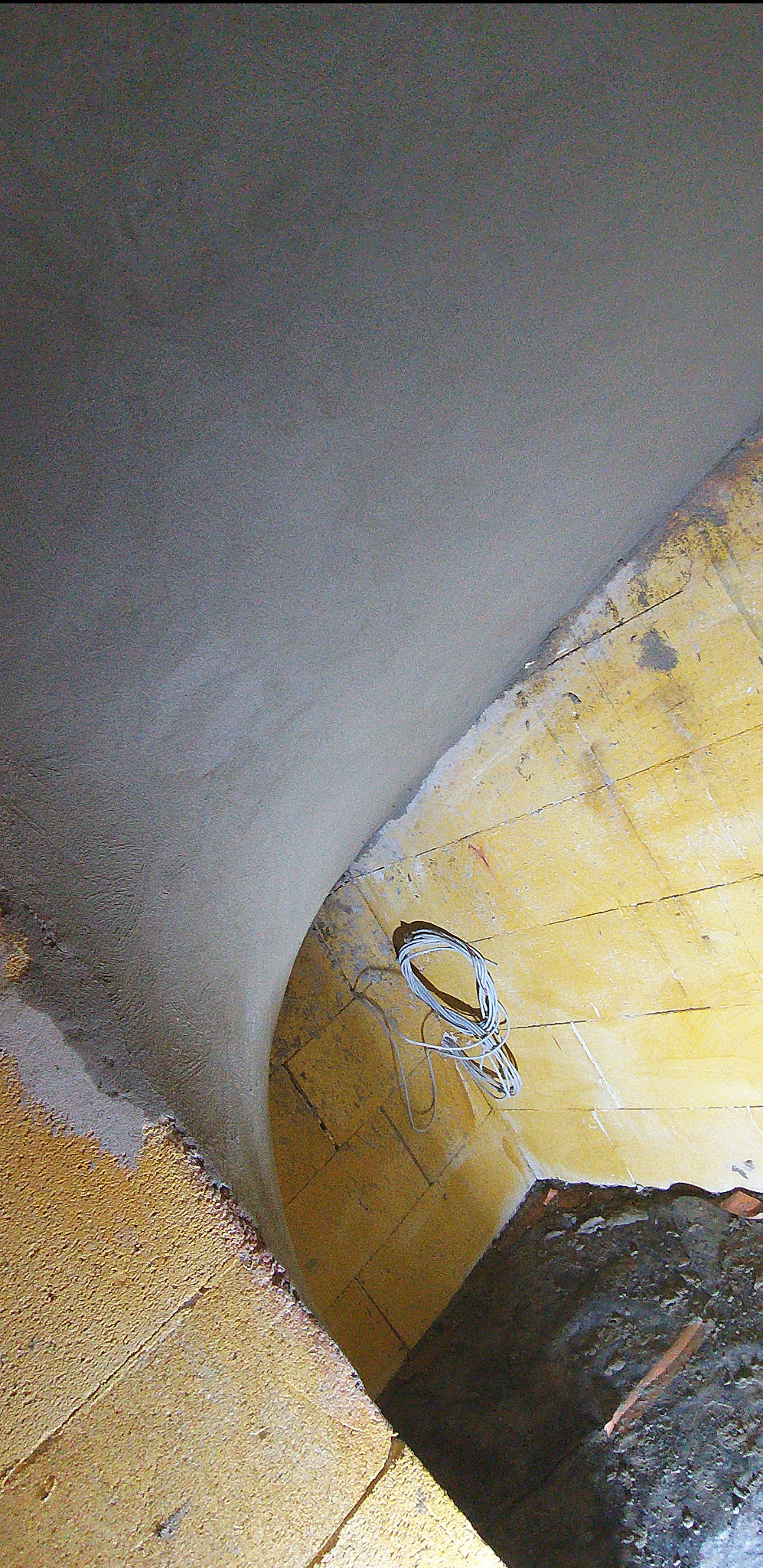 Wnętrze łuku z nałożonym tynkiem maszynowym, widoczne przewody elektryczne i fragment muru z cegły. Ujęcie z dołu, podkreślające krzywiznę i fakturę tynku.