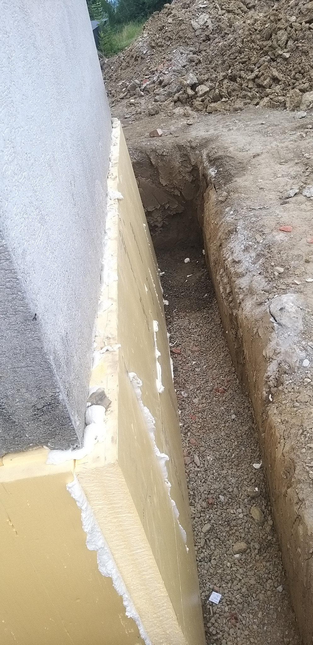 Ocieplenie fundamentu budynku z widoczną izolacją termiczną i wykopem wypełnionym żwirem. Detal łączenia płyt izolacyjnych pianką montażową.