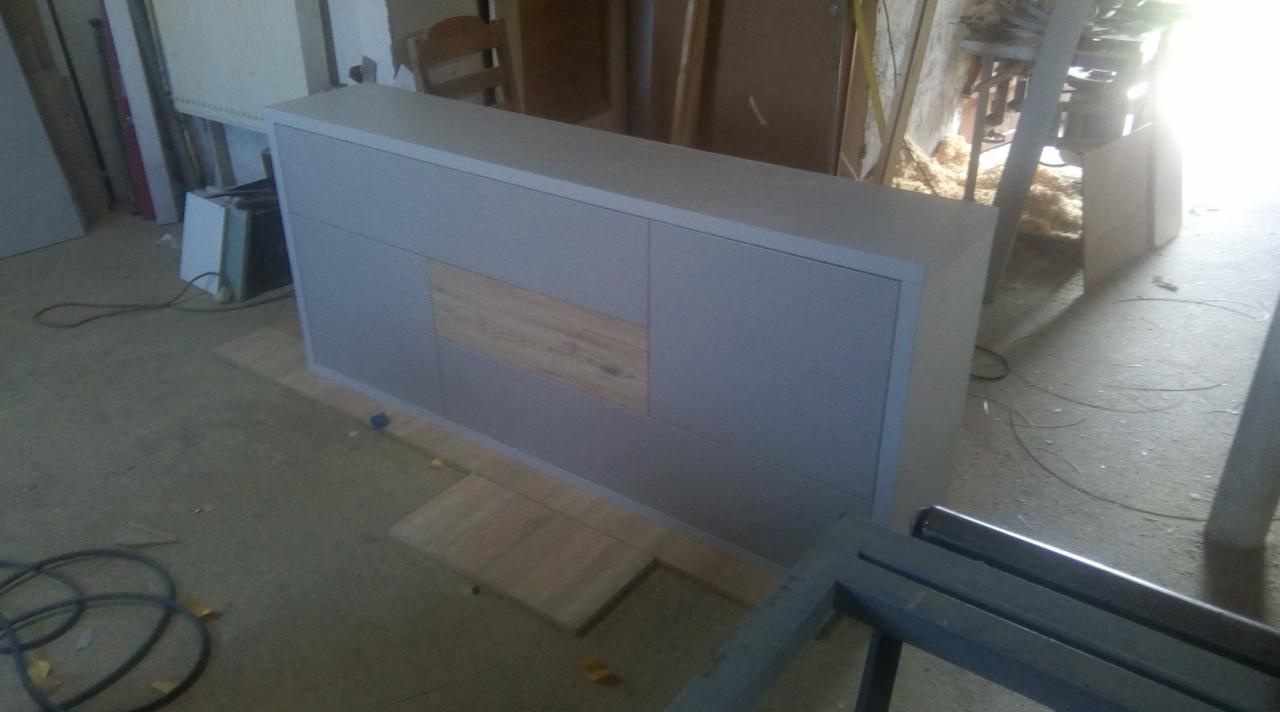 Szara szafka z drewnianym panelem frontowym, w trakcie montażu w warsztacie, widoczne narzędzia i elementy konstrukcyjne.
