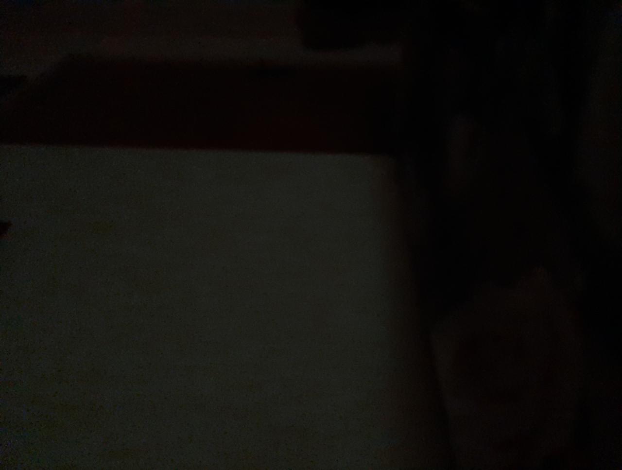 Słabo oświetlony fragment ściany z widocznym zarysem sufitu i elementami w ciemnych odcieniach.