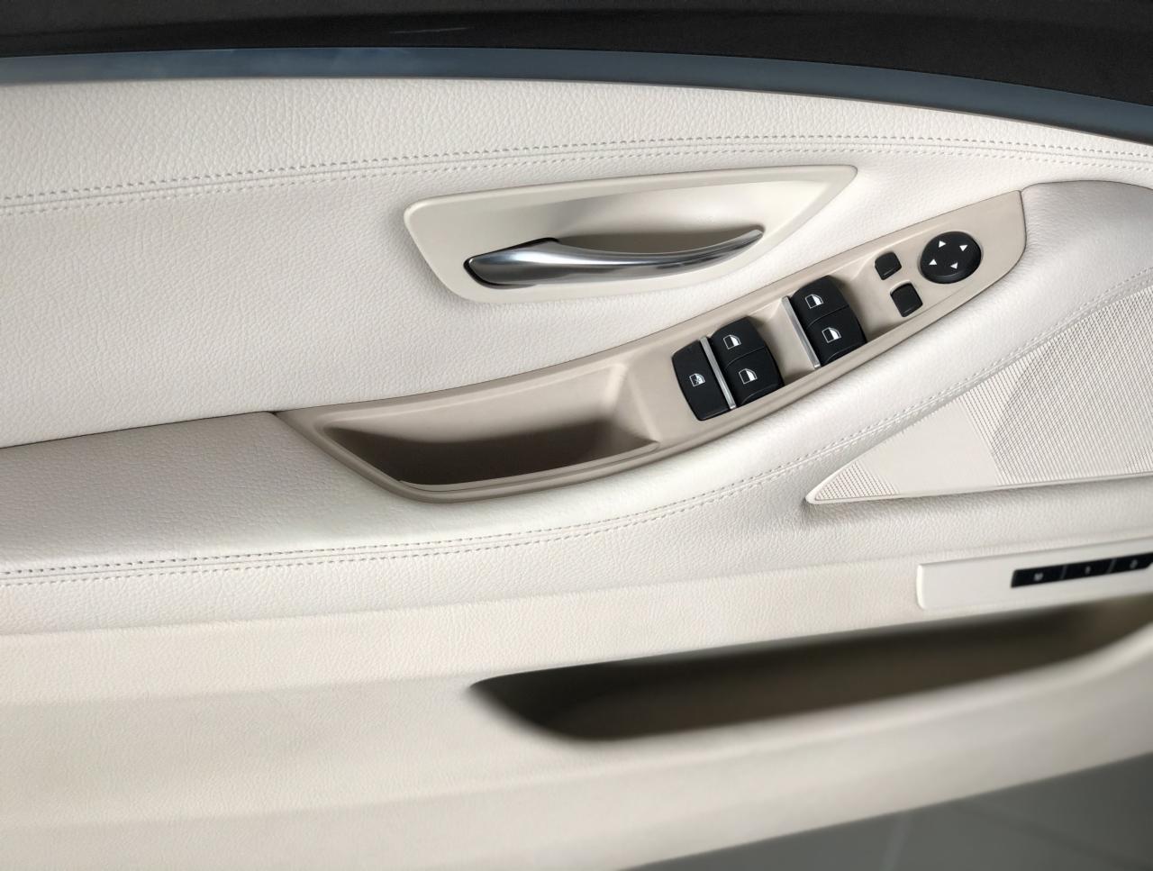 Wnętrze samochodu: beżowy panel drzwi z chromowaną klamką, przyciskami sterowania szybami i lusterkami, widoczne przeszycia na skórze.