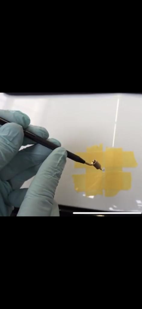 Detailing samochodu: Ręka w lateksowej rękawicy aplikuje punktowo preparat na lakierze, zabezpieczonym taśmą maskującą.