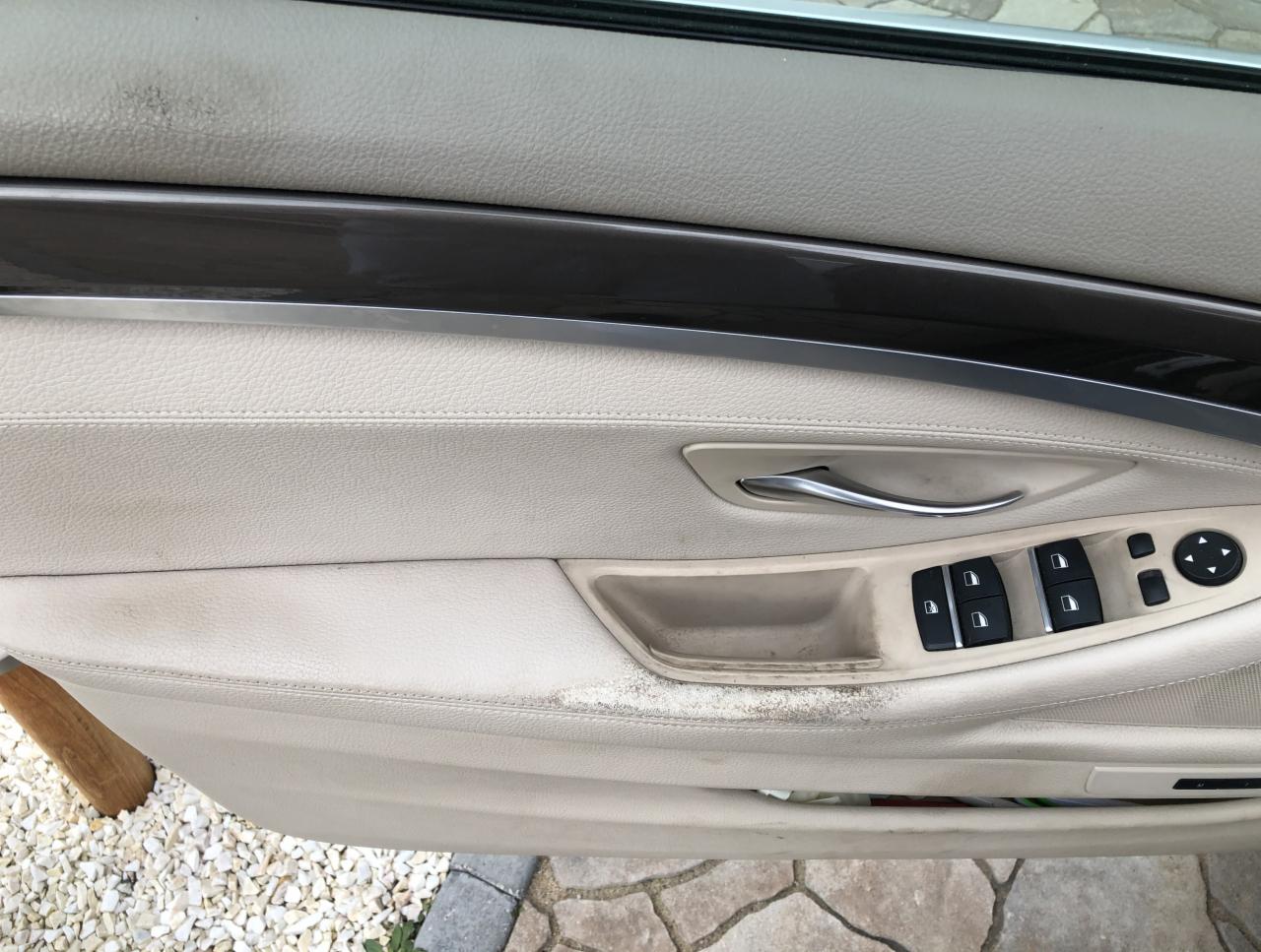 Brudny beżowy panel drzwi samochodu z widocznymi plamami i zabrudzeniami, uchwyt, panel sterowania szybami i boczne lusterka.