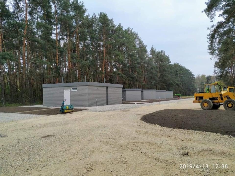 Równanie terenu pod modułowe budynki na żwirowym podłożu, widoczna zagęszczarka wibracyjna i żółta ładowarka teleskopowa w tle lasu.