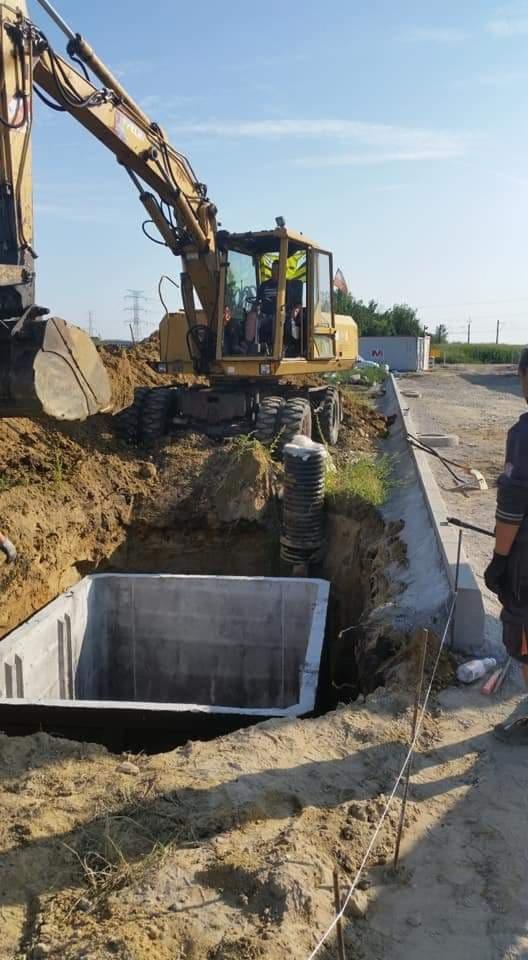 Żółta koparka przygotowuje wykop pod betonowy szambon w Jarosławicach, widoczna betonowa konstrukcja szamba i elementy kanalizacji.