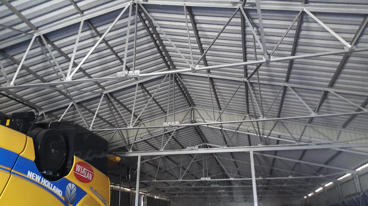 Wnętrze hali z widoczną konstrukcją stalową dachu i fragmentem żółtego kombajnu New Holland