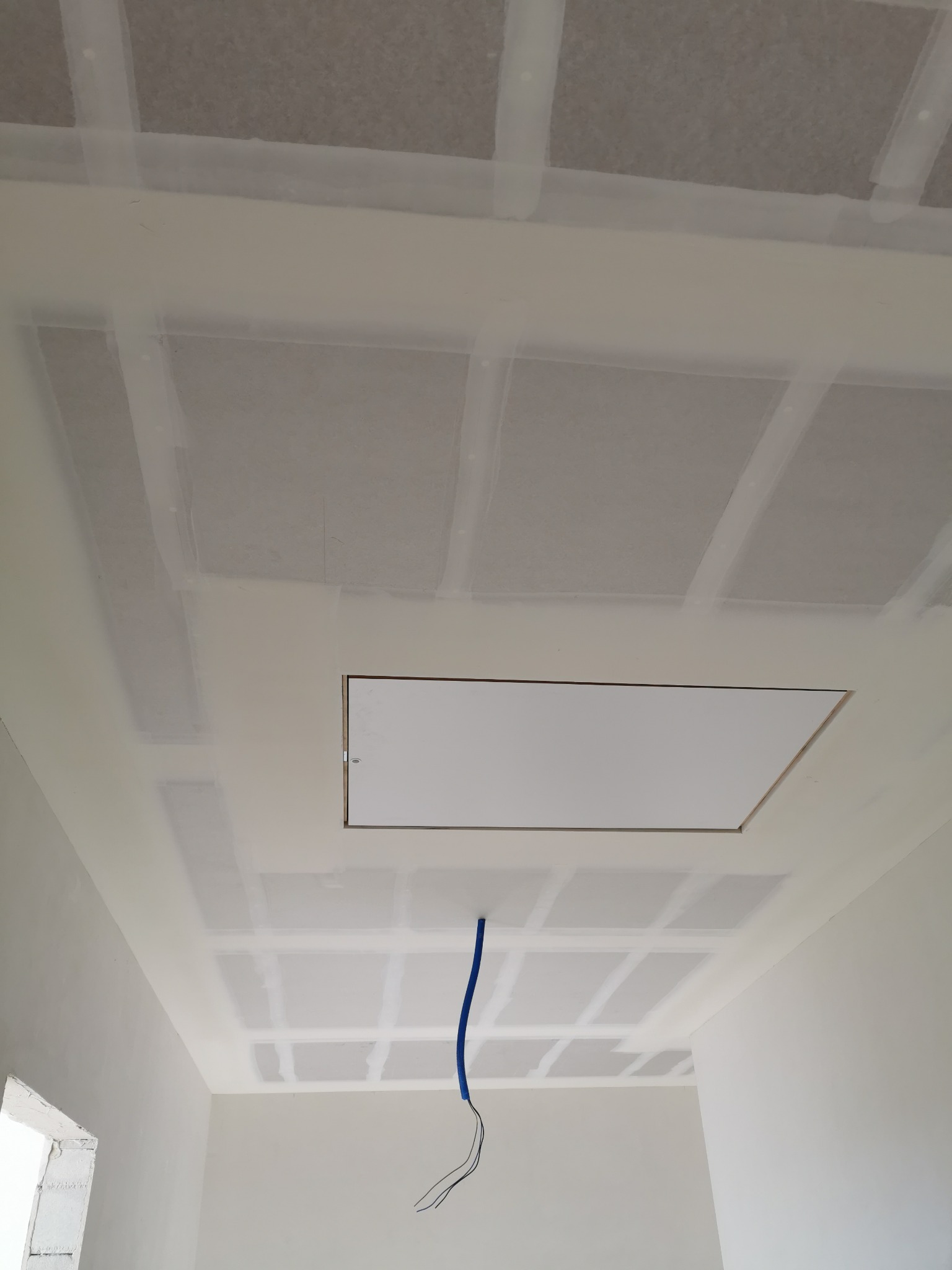 Sufit z płyt kartonowo-gipsowych w trakcie montażu, widoczne łączenia wzmocnione taśmą, otwór rewizyjny i wystające kable.