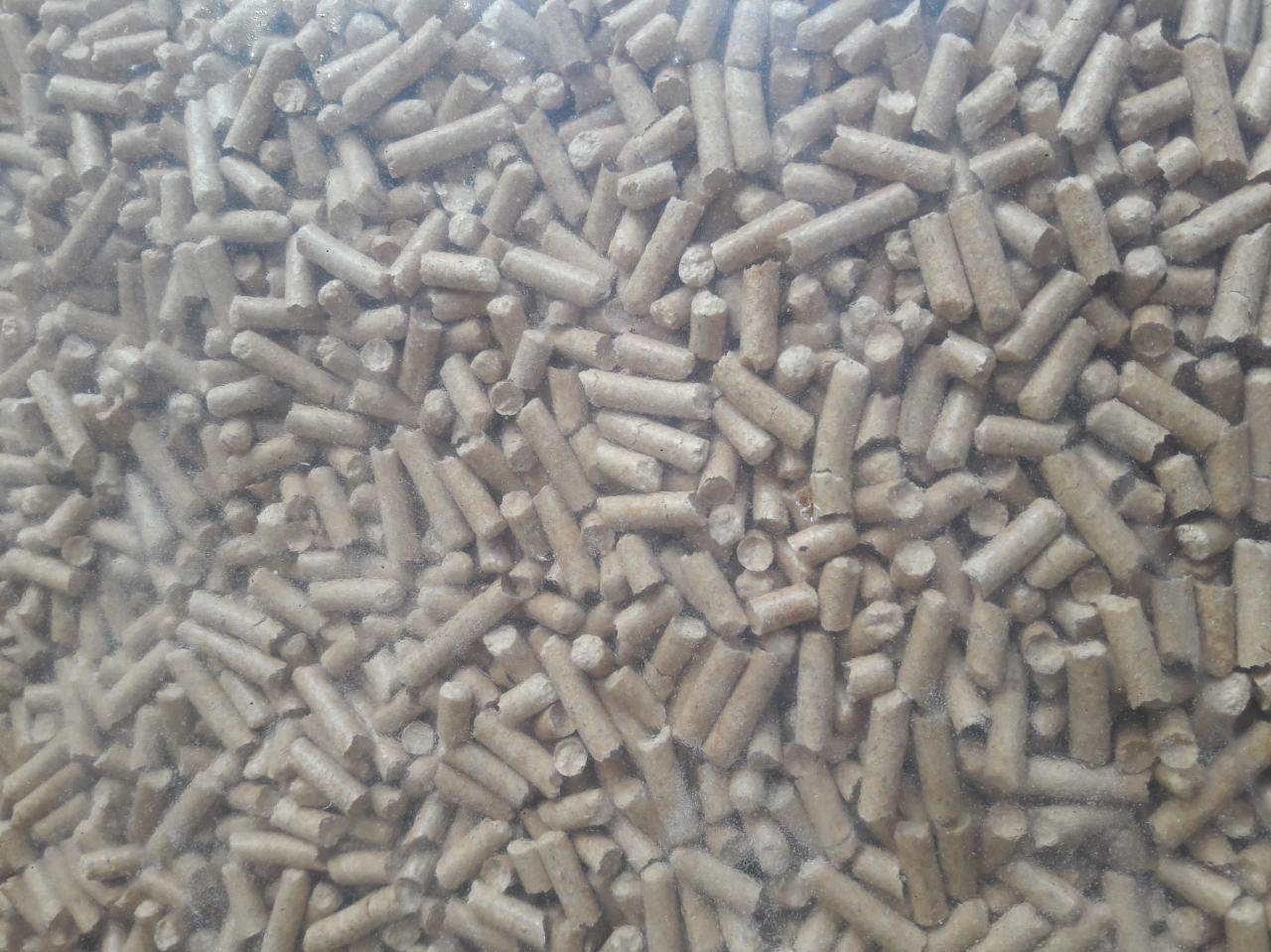 Jasnobrązowe granulki pelletu drzewnego, widoczne przez przezroczyste opakowanie.