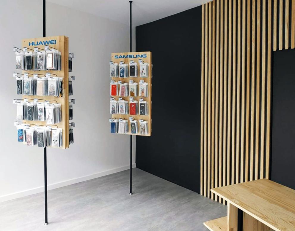 Ekspozycja etui na telefony Huawei i Samsung na drewnianych stojakach w minimalistycznym wnętrzu z czarną ścianą i drewnianą dekoracją.