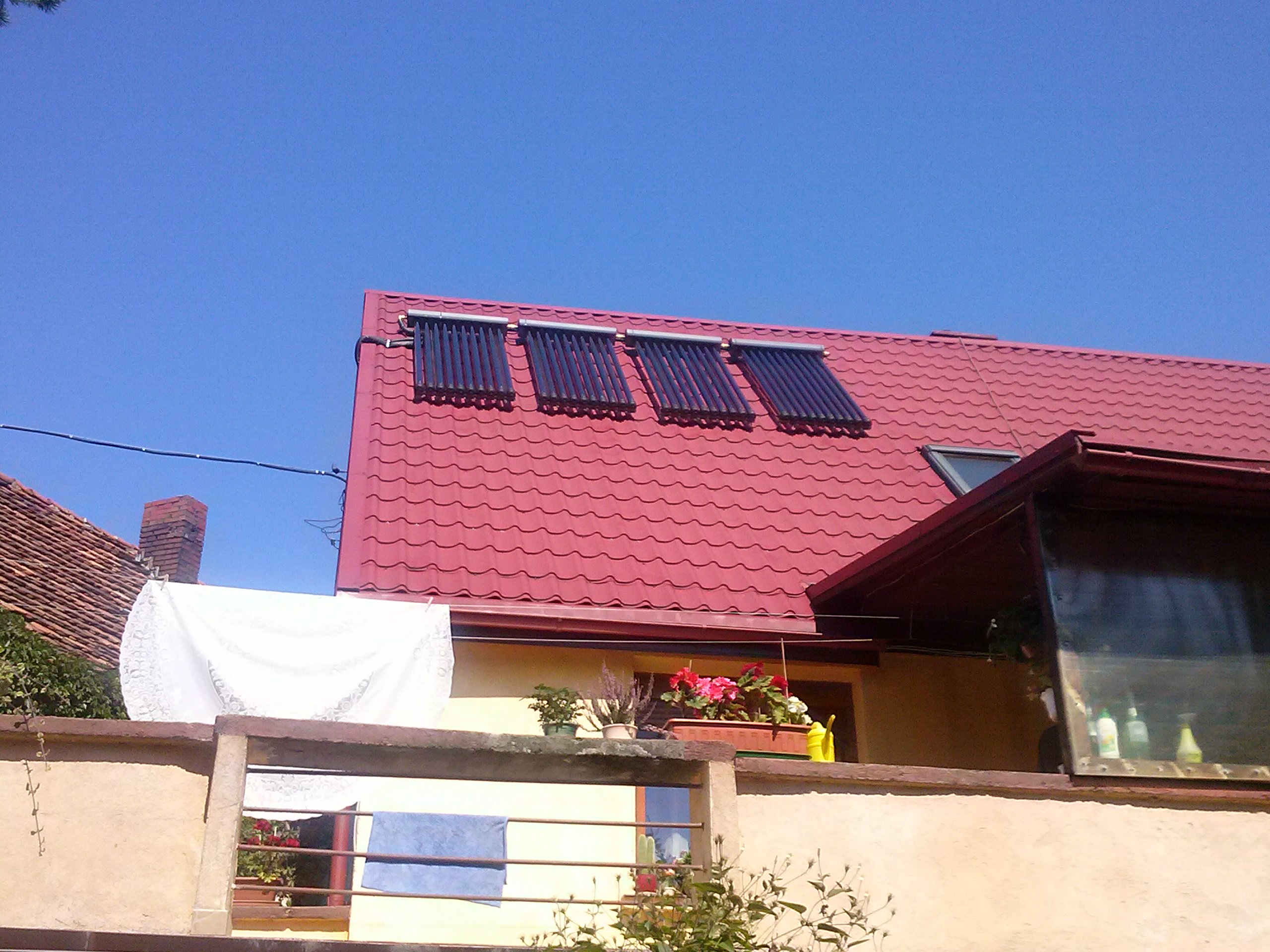 Trzy kolektory słoneczne rurowe zamontowane na czerwonym dachu domu jednorodzinnego w słoneczny dzień. W tle błękitne niebo.