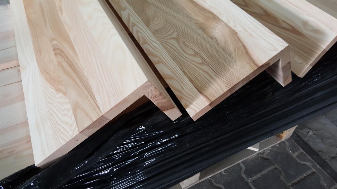 Surowe drewniane stopnie schodowe z widocznym usłojeniem, zabezpieczone folią, czekające na montaż.