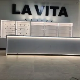 Białe szafy na wymiar z podświetleniem LED i napisem 'LA VITA' na ścianie, widok z niskiego kąta.