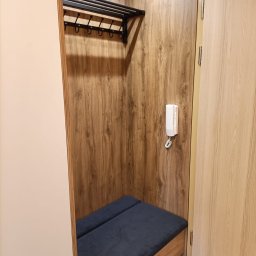 Teta Piotr Jóźwiak - Wnęka garderoby z drewnianym wykończeniem, wyposażona w wieszak na ubrania, tapicerowane siedzisko i domofon na ścianie.