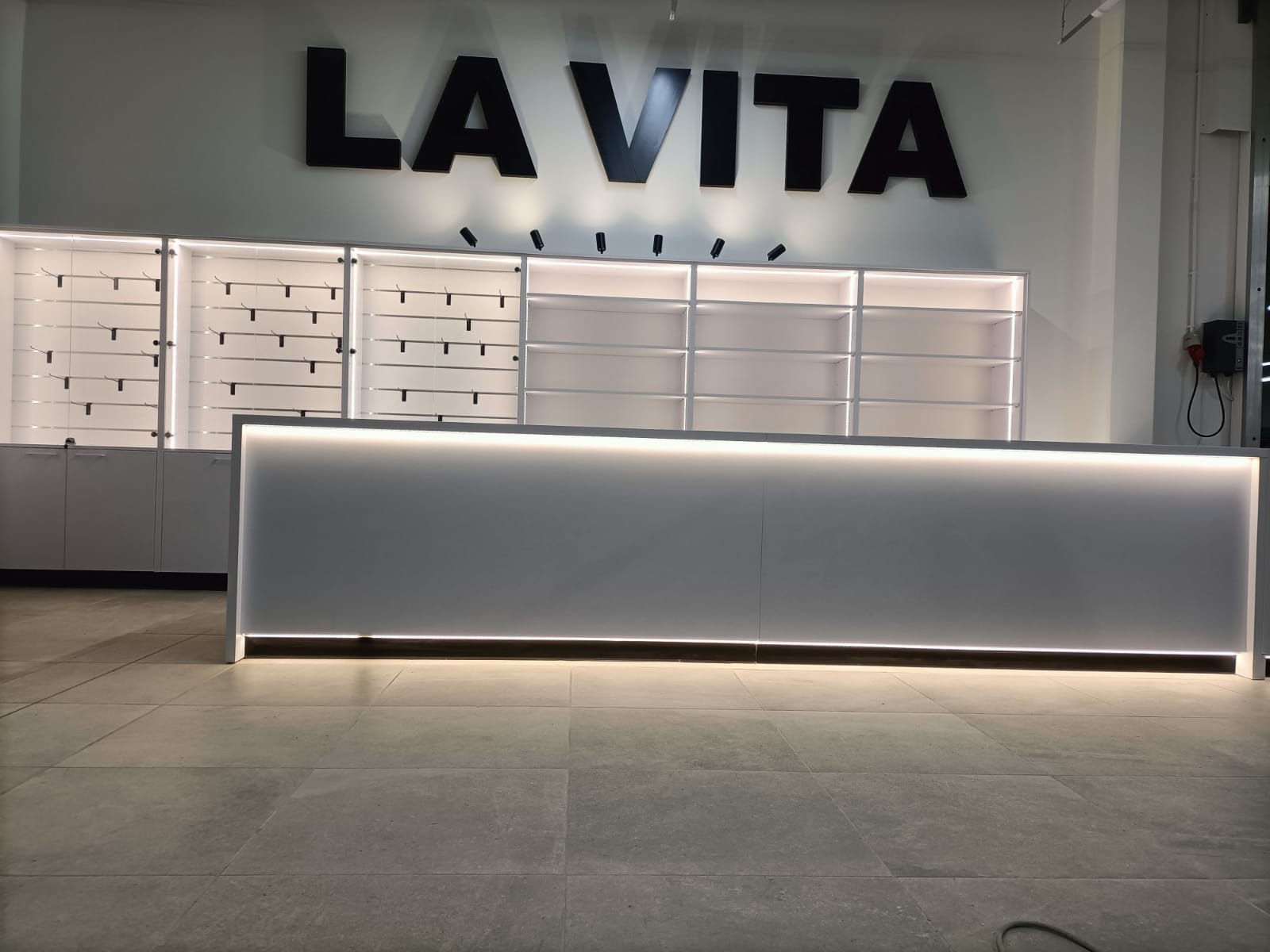 Białe szafy na wymiar z podświetleniem LED i napisem 'LA VITA' na ścianie, widok z niskiego kąta.