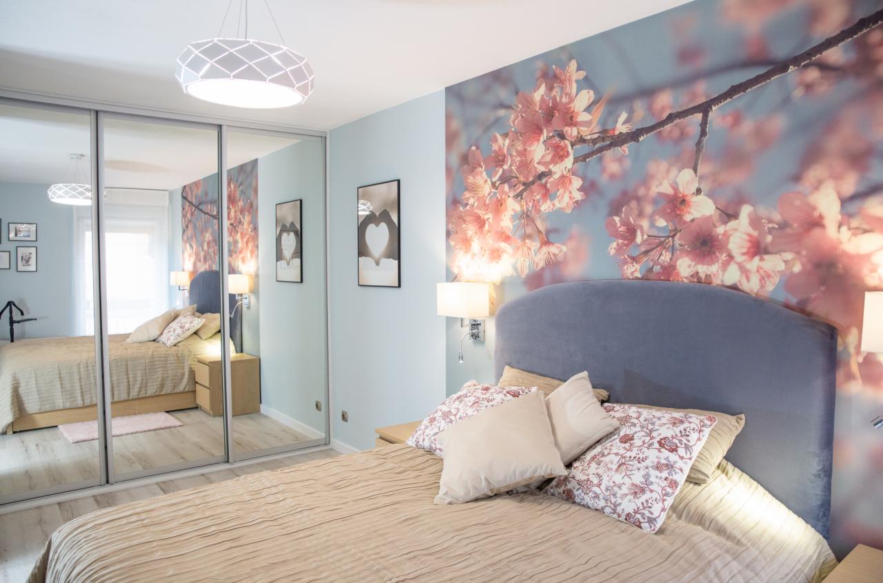 Jasna sypialnia z łóżkiem, tapetą z motywem kwitnącej wiśni i szafą z lustrzanymi drzwiami przesuwnymi.