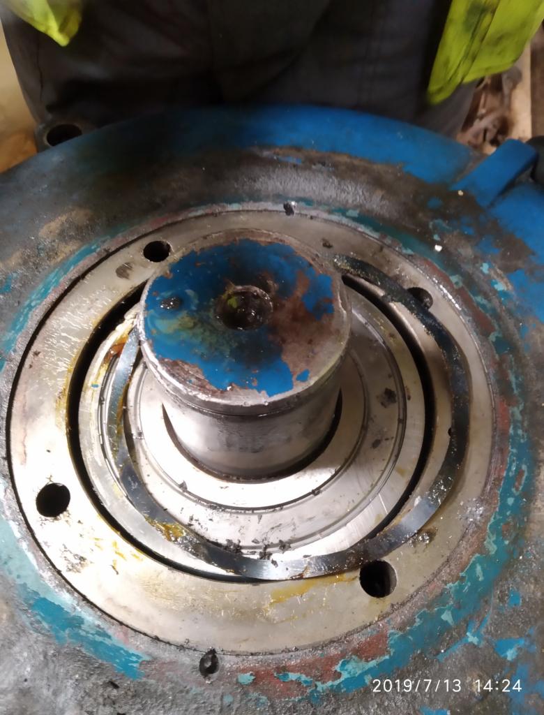 Otwarty mechanizm maszyny z widocznymi zużytymi łożyskami i elementami metalowymi, ślady smaru i zabrudzeń, ujęcie z góry.