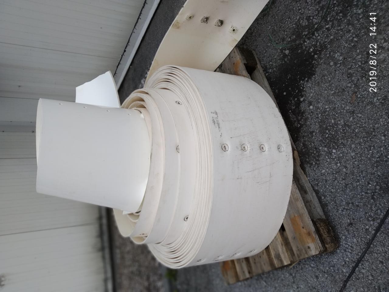 Rolka białego, elastycznego tworzywa sztucznego z otworami na śruby, leżąca na drewnianej palecie, prawdopodobnie element maszyny rolniczej lub przemysłowej.