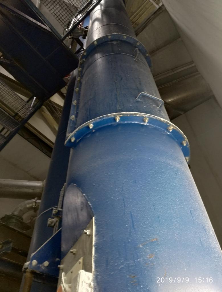 Wysoki, pionowy, niebieski silos przemysłowy z widocznymi śrubami i elementami mocującymi, umieszczony wewnątrz hali, sfotografowany z dołu pod kątem, z datą i godziną w prawym dolnym rogu.