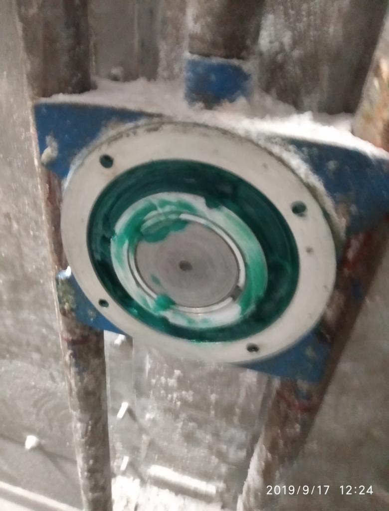 Fragment maszyny z nałożonym smarem w kolorze zielonym, widoczne ślady białego pyłu. Element mocowany do niebieskiej podstawy.