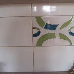 Białe, poziomo żłobkowane płytki ścienne z zielono-niebieskim wzorem geometrycznym na jednej z płytek.