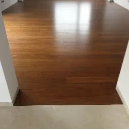 Błyszcząca, ułożona podłoga z ciemnego drewna bambusowego w nowym mieszkaniu, widok z progu na jasne wnętrze.