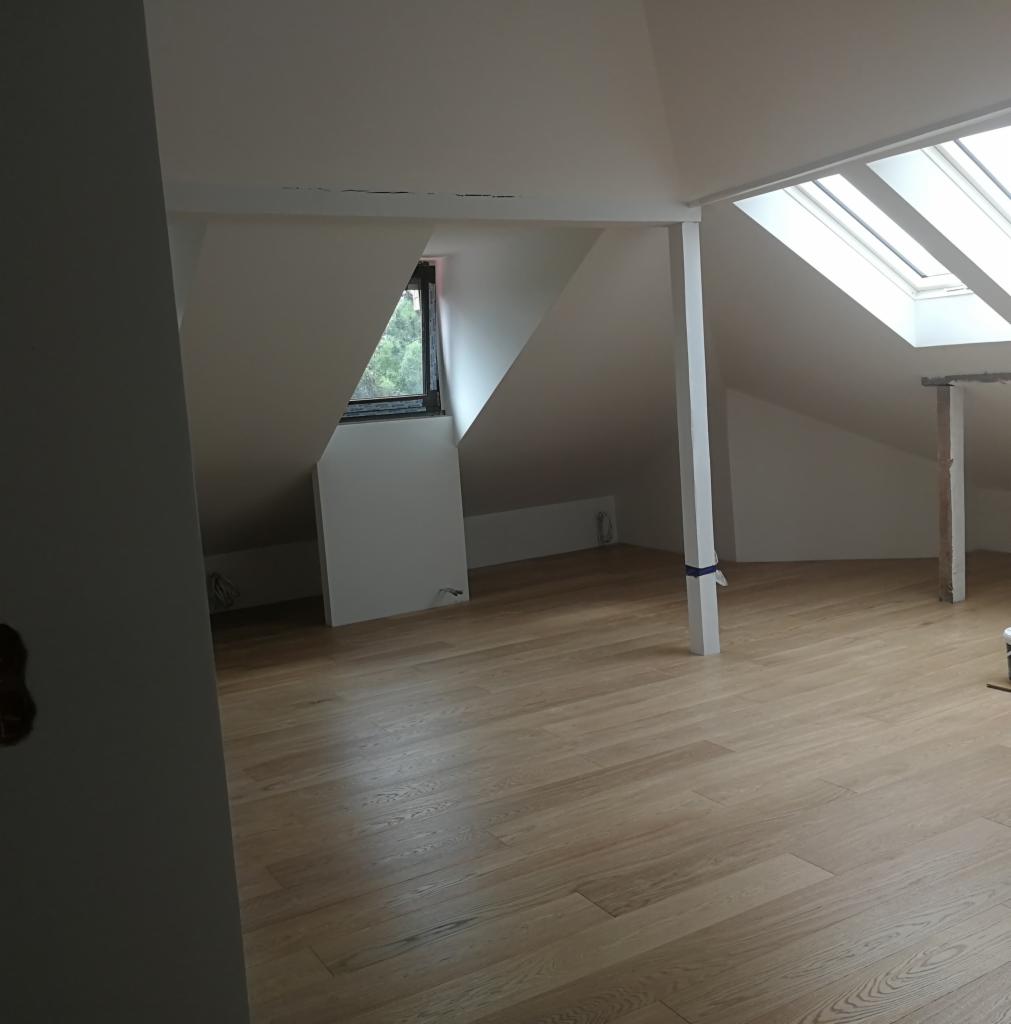 Jasna, drewniana podłoga w nowym, przestronnym pokoju na poddaszu z oknami dachowymi i białymi ścianami.