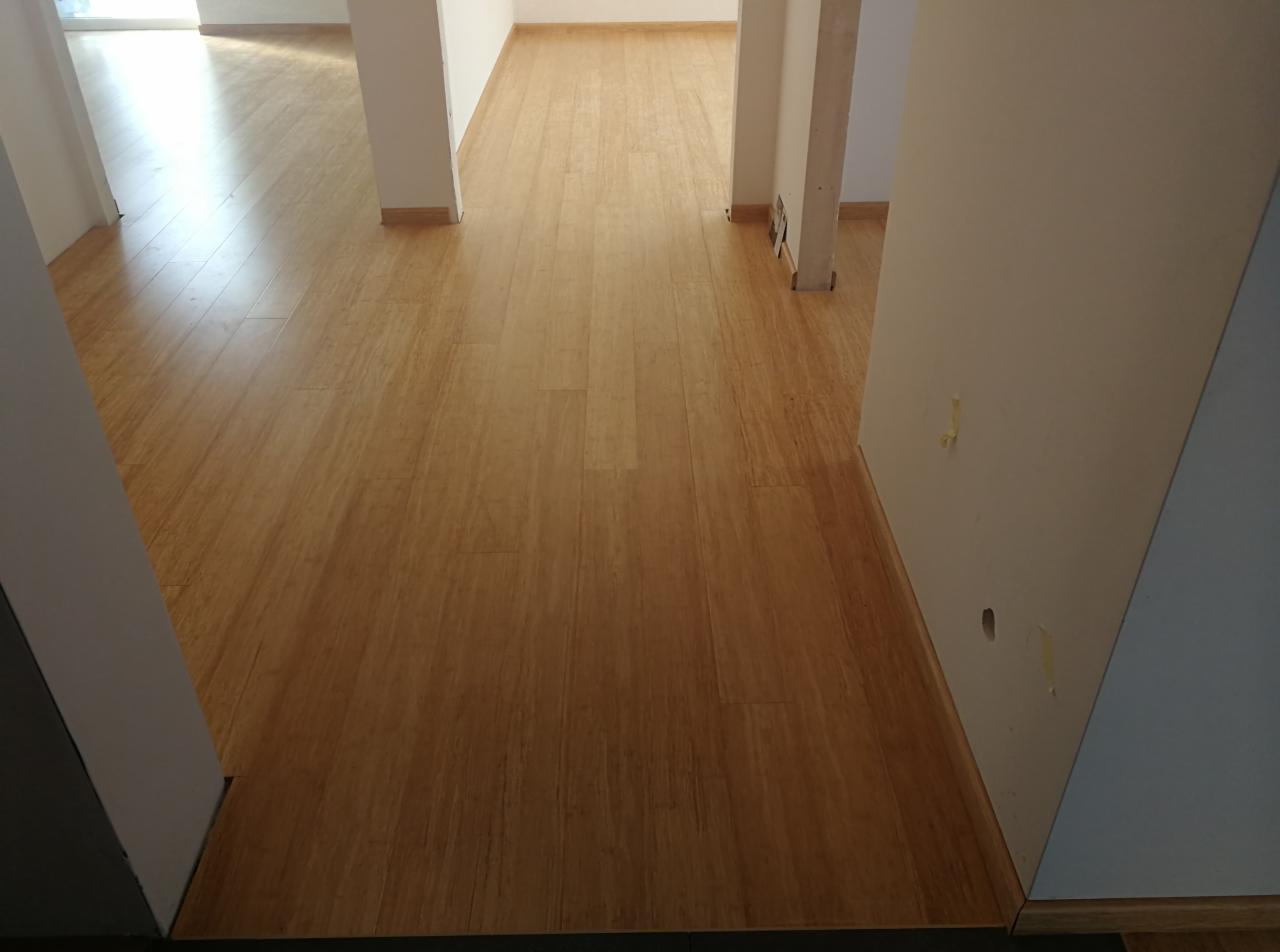 Jasna, drewniana podłoga w nowym mieszkaniu, widok z perspektywy wejścia, białe ściany i filary w tle, widoczne niedoskonałości na ścianie.