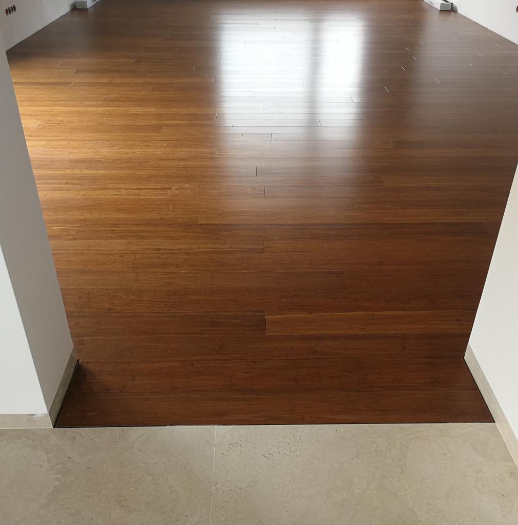 Błyszcząca, ułożona podłoga z ciemnego drewna bambusowego w nowym mieszkaniu, widok z progu na jasne wnętrze.