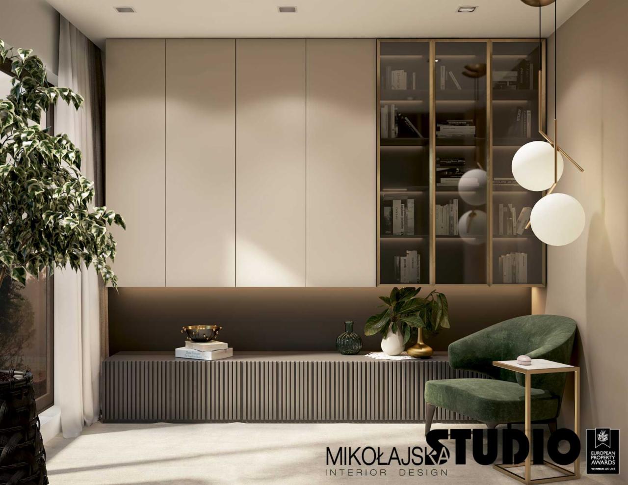 Nowoczesny salon z zabudową meblową w odcieniach beżu i brązu, przeszklona witryna z książkami, fotel obity zielonym welurem oraz designerska lampa z białymi kulami.