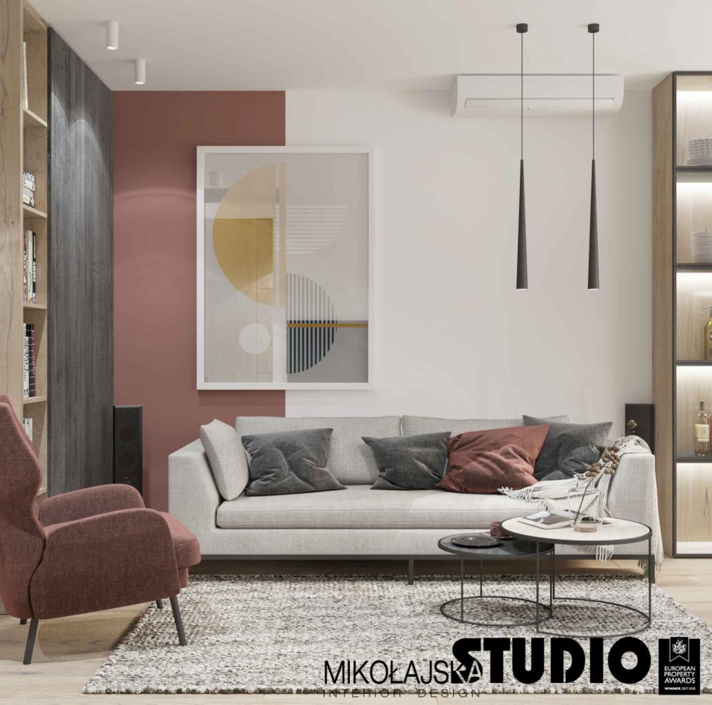 Nowoczesny salon z szarą sofą, abstrakcyjnym obrazem na ścianie w kolorze terakoty i białym, oraz wiszącymi lampami w kształcie stożków.