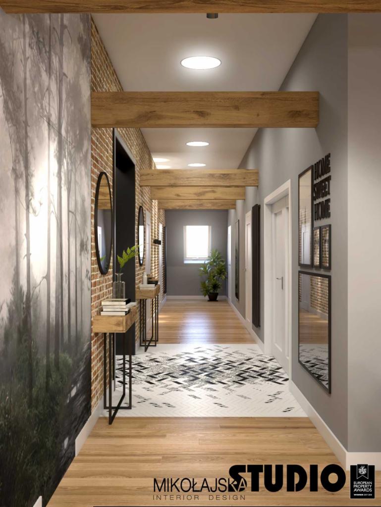Długi korytarz z drewnianymi belkami stropowymi, tapetą z motywem leśnym, ceglaną ścianą i konsolami z książkami oraz lustrami.