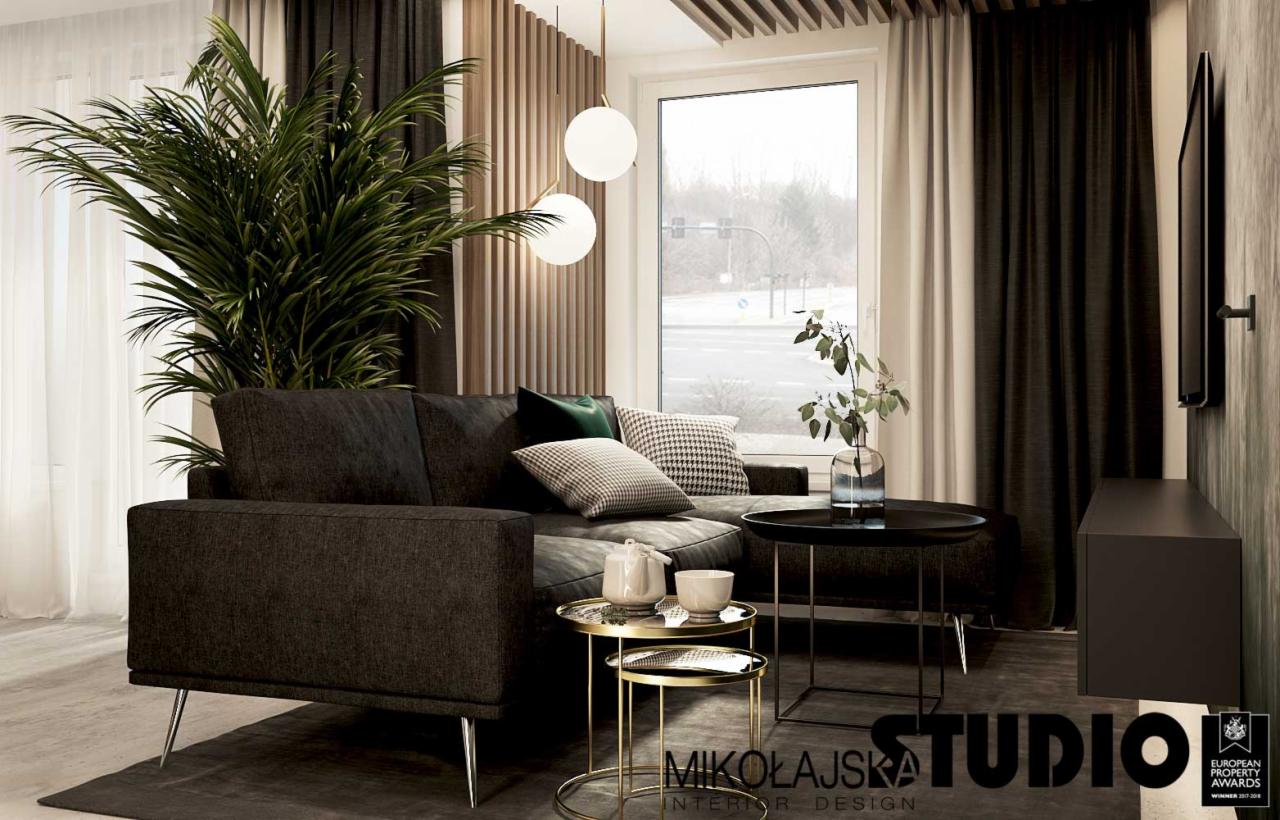 Nowoczesny salon z ciemną sofą na metalowych nóżkach, okrągłymi stolikami kawowymi w kolorze złota i czerni, dużą rośliną doniczkową i dekoracyjnymi poduszkami, oświetlony wiszącymi lampami kulami.