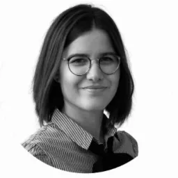 Portret kobiety w okularach i koszuli w paski, uśmiechającej się, na białym tle.