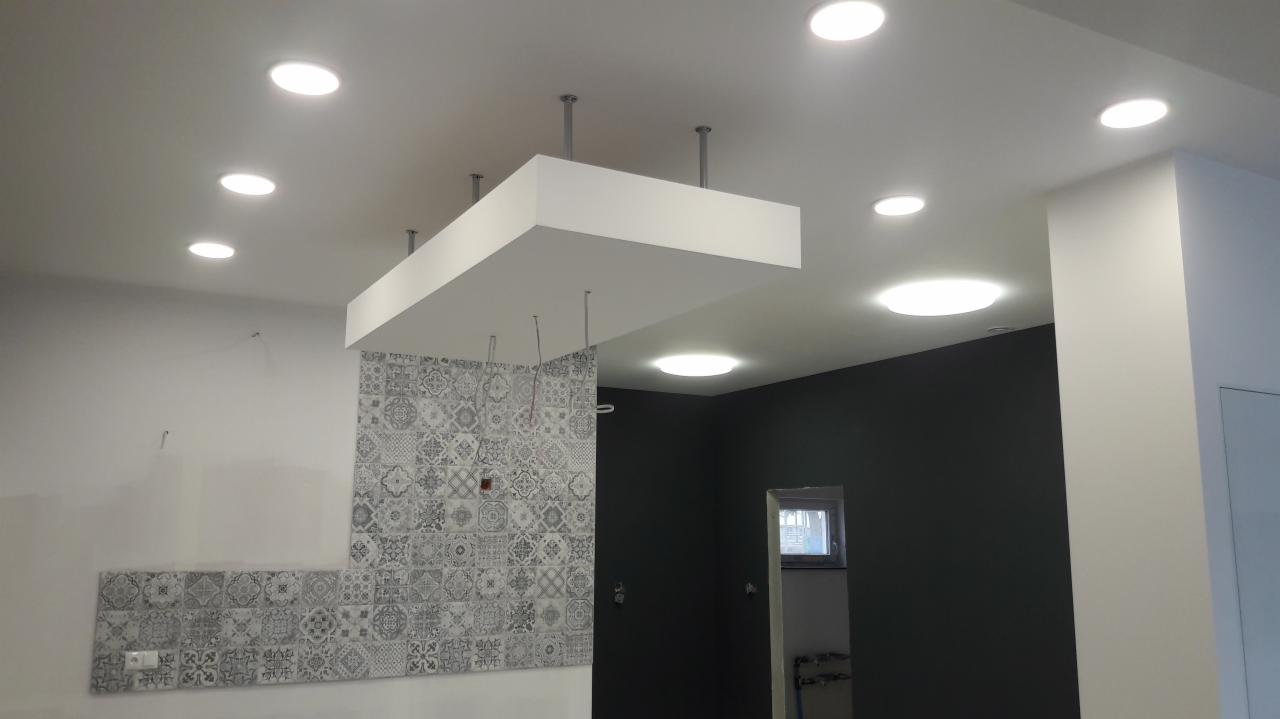 Wnętrze w trakcie remontu: widoczne płytki dekoracyjne na ścianie, podwieszany sufit z oświetleniem LED oraz świeżo pomalowana ściana w kolorze grafitowym
