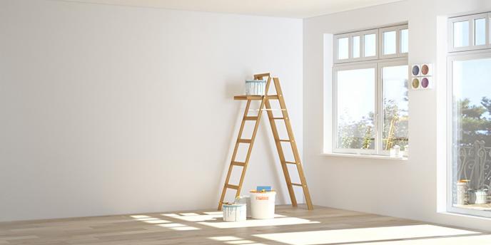 Jasne wnętrze w trakcie prac: drewniana drabina, puszki z farbą i próbki kolorów na ścianie obok okna.