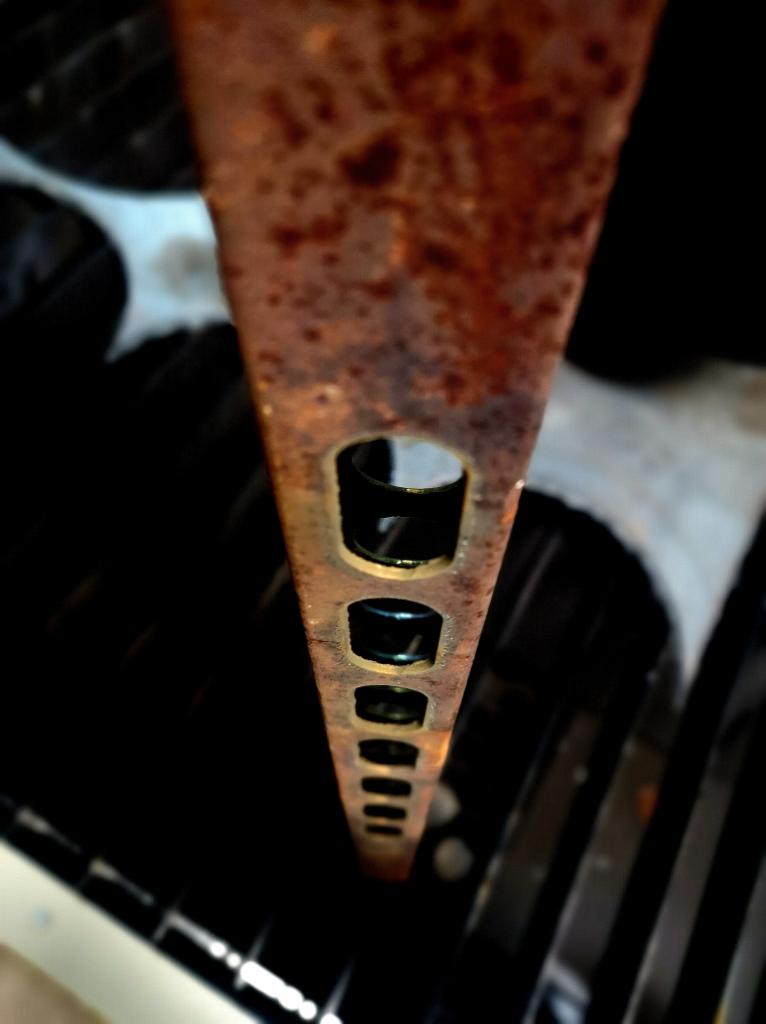 Zardzewiała, perforowana listwa stalowa ustawiona pionowo na tle ciemnych, okrągłych elementów maszynowych.