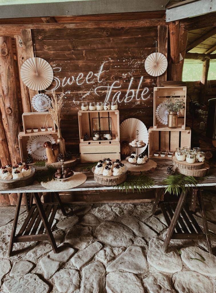 Rustykalny stół ze słodkościami: mini bezy z owocami, czekoladowe praliny, desery w słoiczkach, dekoracje z drewna i papieru.