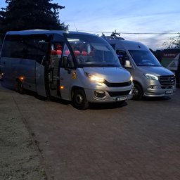 Firma Przewozowa Skbus Sp.j Stachura - Dwa srebrne busy zaparkowane obok siebie na brukowanej powierzchni o zmierzchu, z otwartymi drzwiami w jednym z nich, ukazując czerwone fotele wewnątrz.