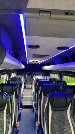 Wnętrze autobusu z czarno-szarymi skórzanymi siedzeniami, oświetleniem LED i schodkami w przejściu.