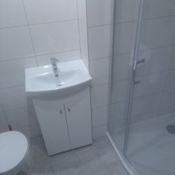 Mariusz Mioduszewski - Nowoczesna, biała umywalka z szafką w łazience po remoncie w Zambrowie, widoczna kabina prysznicowa w tle.