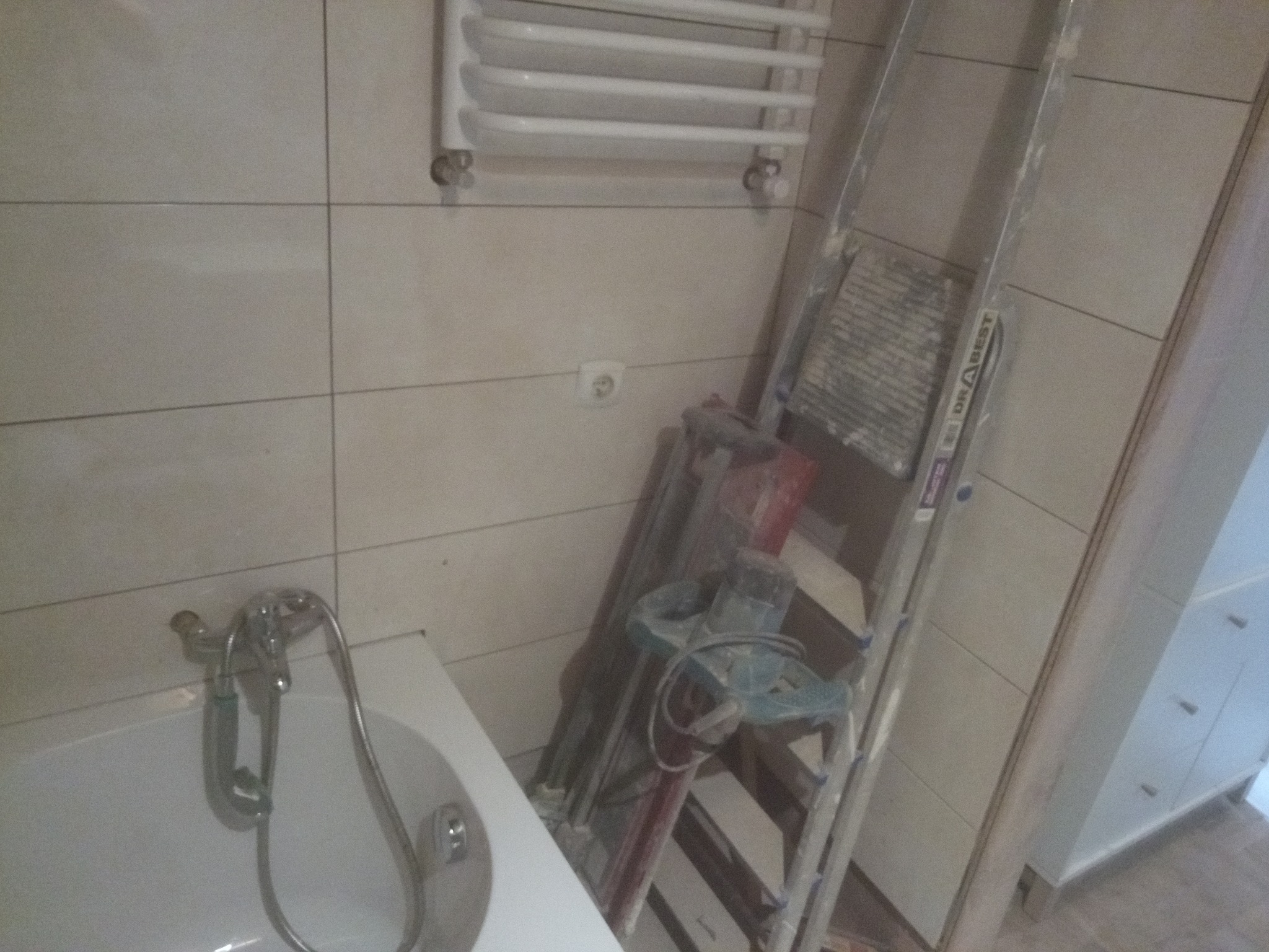 Łazienka w trakcie remontu w Zambrowie: widoczna wanna z baterią, grzejnik drabinkowy na ścianie z płytek, drabina oparta o ścianę i narzędzia budowlane w tle, sugerujące prace wykończeniowe.