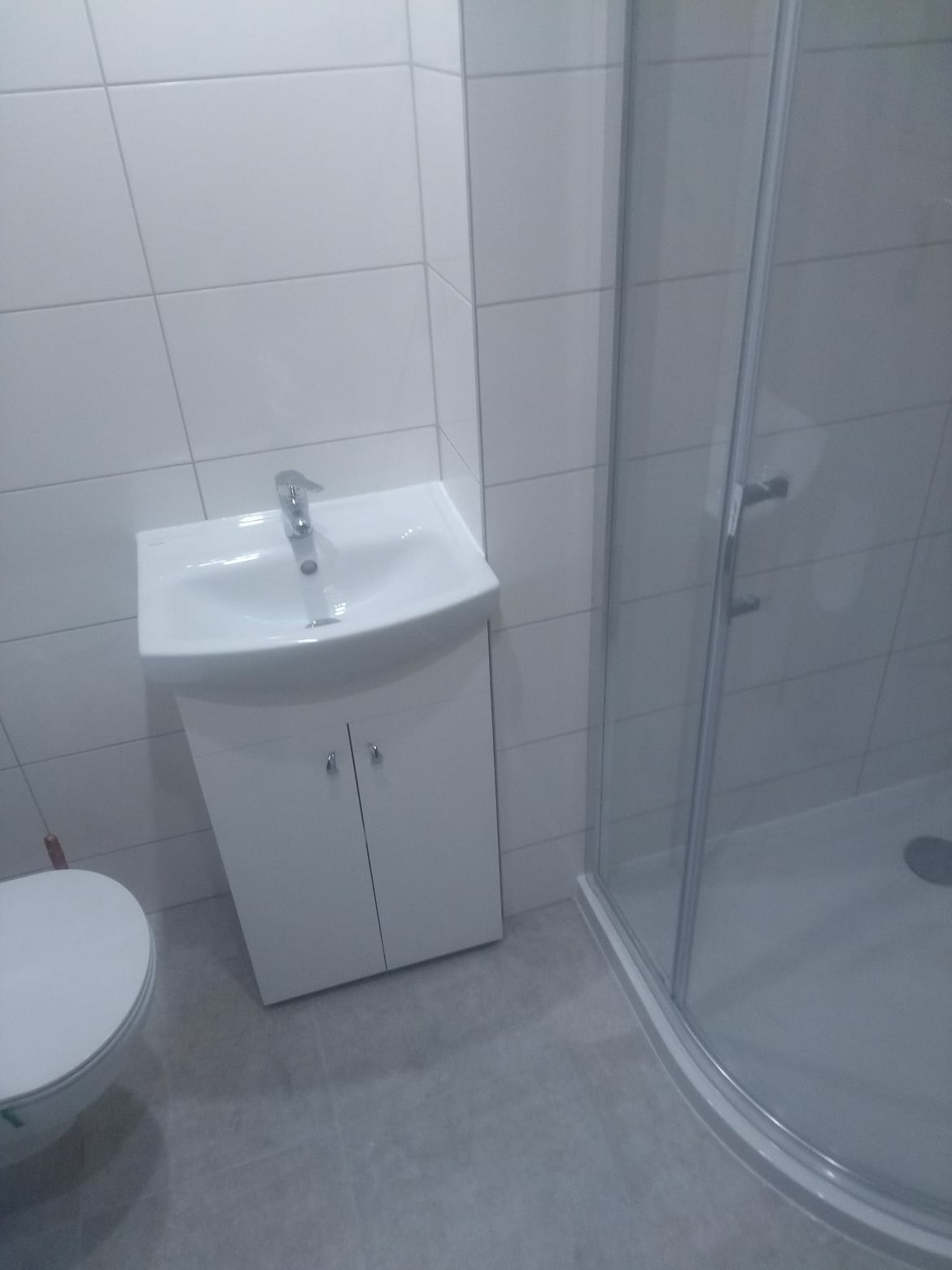 Nowoczesna, biała umywalka z szafką w łazience po remoncie w Zambrowie, widoczna kabina prysznicowa w tle.